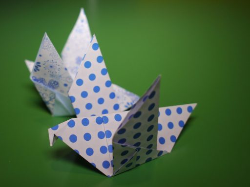 Kind dat aan tafel een origamifiguur aan het vouwen is met een vel wit papier