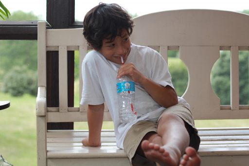 Kind dat water drinkt op een warme zomerdag buiten in de schaduw