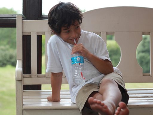 Kind dat water drinkt op een warme zomerdag buiten in de schaduw